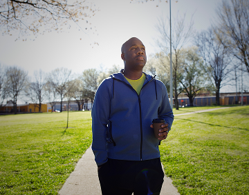 A Person Walking Outdoors on a Walking Path, Holding a Cup of Coffee